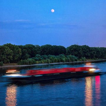 Beginnende Mondfinsternis mit rotem Mars über dem Rhein als ein Schiff ein Containerschiff vorbeifährt