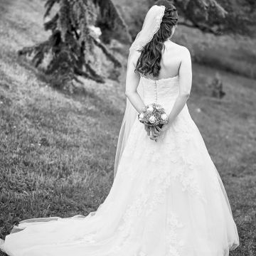 Braut mit langem weißen Hochzeitskleid von hinten in schöner Landschaft in schwarzweiß